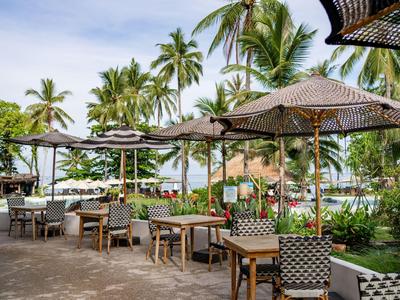 Freiluftrestaurant mit Tischen, Stühlen und Sonnenschirmen nahe tropischem Strand.