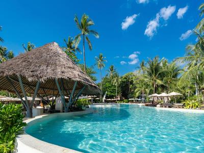 Großer Pool mit klarem Wasser, Palmen und Sonnenschirmen in tropischer Hotelanlage.