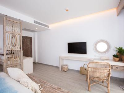 Helles Zimmer mit Holzboden, Rattanmöbeln, TV an der Wand und runder Spiegel am Schreibtisch.