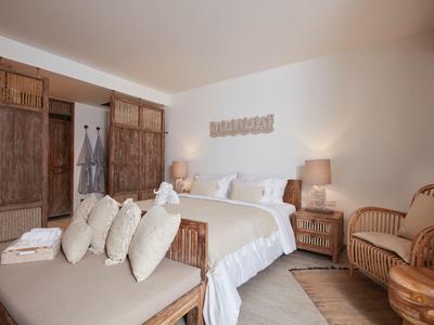 Helles Schlafzimmer mit Holzmöbeln, gemütlichem Bett, Sitzbank mit Kissen und natürlicher Beleuchtung.