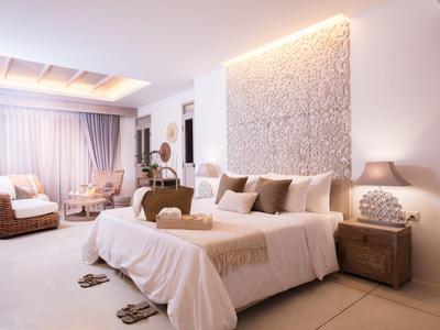 Hell eingerichtetes Schlafzimmer mit großem Bett, weißer Wanddekoration und Rattanstühlen.