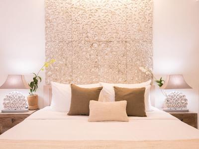 Modernes Schlafzimmer mit beigem Bett, braunen Kissen, zierlichen Nachttischlampen und dekorativer Wand.