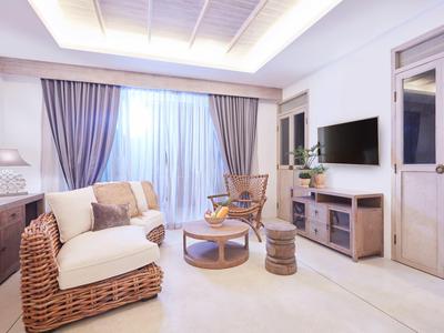Helles Wohnzimmer mit Rattansofa, Holzkommode, Couchtisch, Sessel und großes Fenster mit Vorhängen.