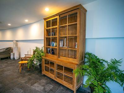 Heller Raum mit Holzbibliothek, zwei Stühlen und grünen Pflanzen an einer hellblauen Wand.