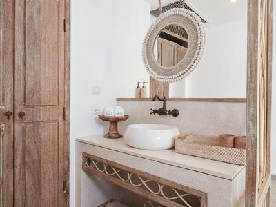 Helles Badezimmer mit rustikalem Holzschrank, rundem Spiegel und weißen Waschbecken auf Steintheke.