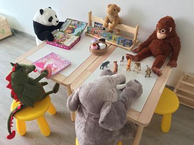 Kleiner Kindertisch mit gelben Stühlen, Holzspielzeug, Tierfiguren und Plüschtiere in hellem Raum.