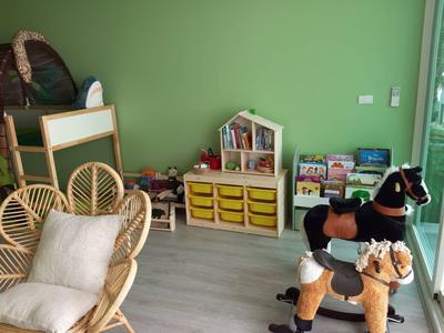 Kinderspielecke mit Holzmöbeln, bunten Aufbewahrungsboxen, Spielzeugpferden und grün gestrichener Wand.