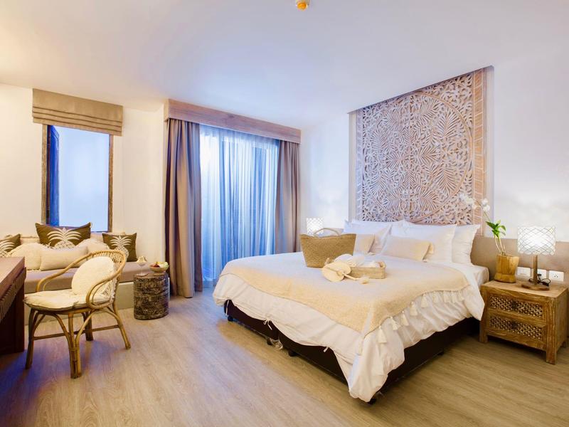 Jasny pokój hotelowy z dużym łóżkiem, biurkiem i oknem z zasłonami.