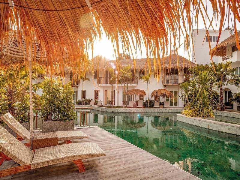 Strefa basenowa hotelu z leżakami i tropikalną dekoracją o zachodzie słońca.