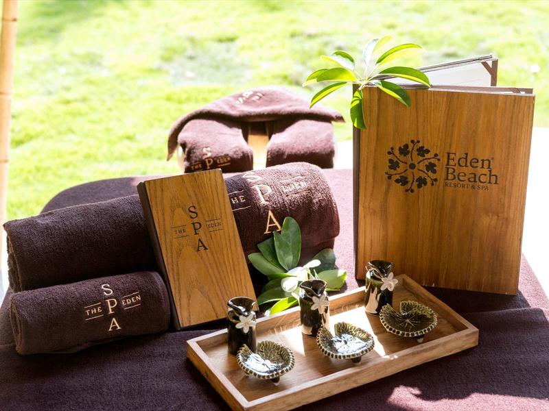 Strefa spa z brązowymi ręcznikami, roślinami i menu Eden Spa na drewnianym stole.