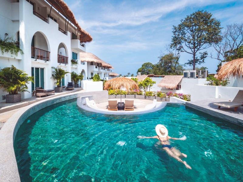 Osoba pływa w hotelowym basenie z leżakami i palmami w słoneczny dzień.