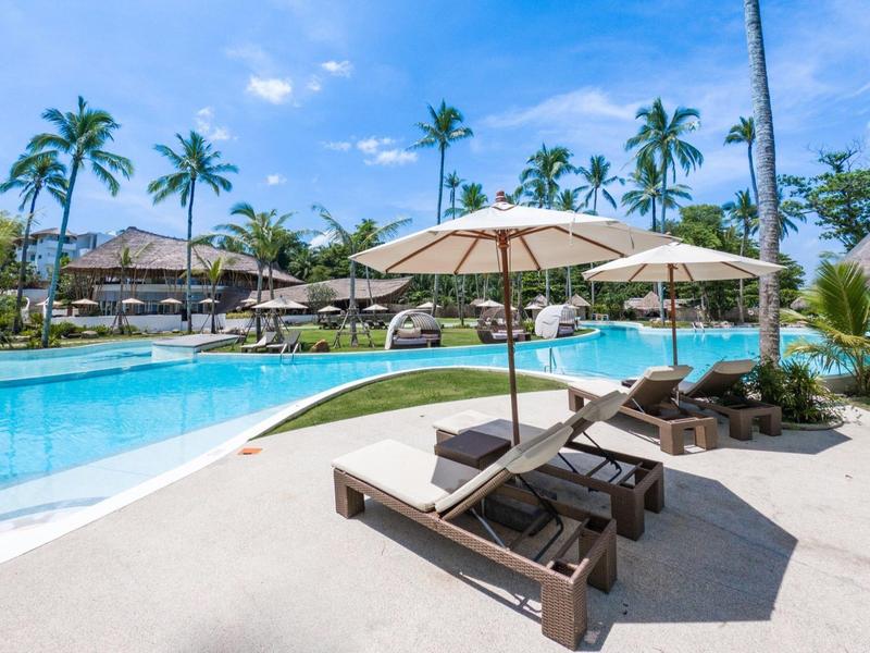 Strefa basenowa z leżakami i parasolami w tropikalnym hotelu pod bezchmurnym niebem.