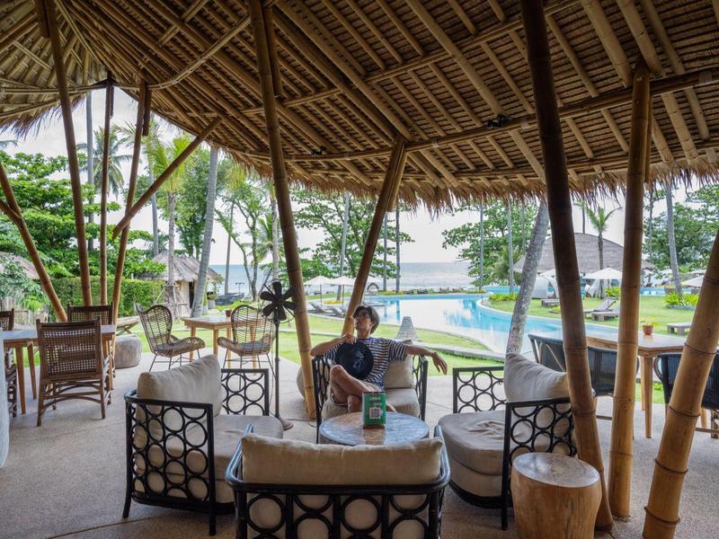 Zadaszony salon z bambusowymi meblami z widokiem na tropikalny basen i palmy