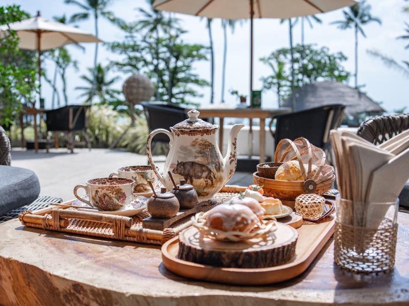Rustykalny drewniany stół z herbatą, ciastkami i serwetkami na zewnątrz pod palmami.