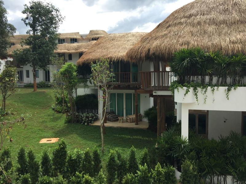 Budynek hotelowy z dachami krytymi strzechą otoczony trawą i drzewami pod zachmurzonym niebem.