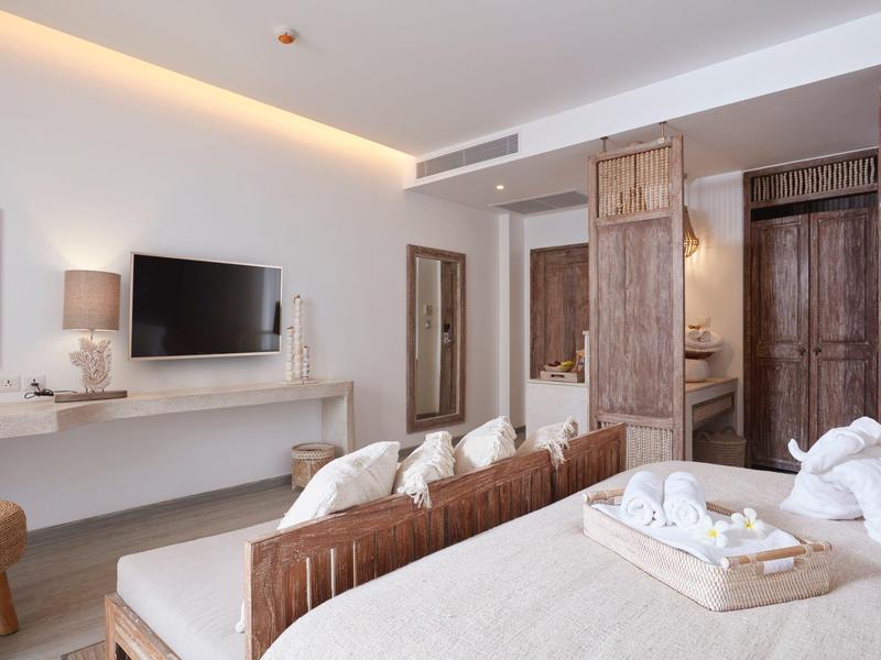 Jasny pokój hotelowy z podwójnym łóżkiem, częścią wypoczynkową, telewizorem i otwartą garderobą.