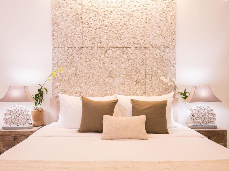 Jasna sypialnia z dużym łóżkiem, ozdobnymi poduszkami i dziełem sztuki za zagłówkiem.