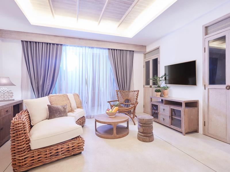 Jasny salon z wiklinowym fotelem, sofą, stolikiem kawowym i zasłonami przed dużymi oknami.