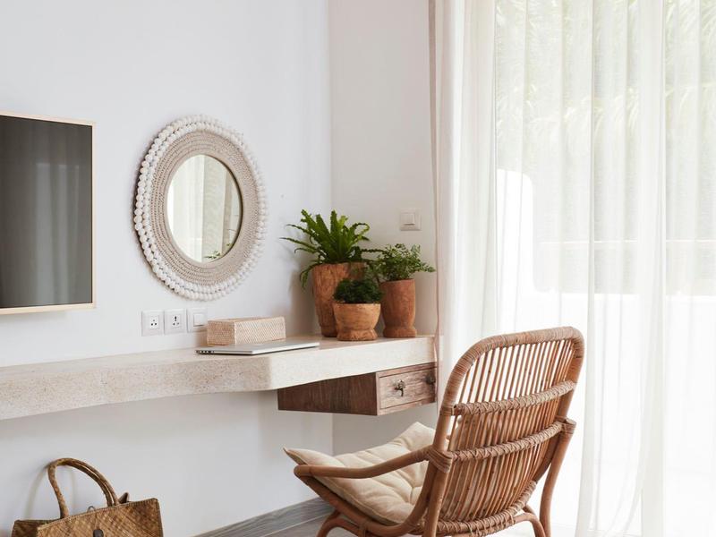 Jasny pokój z wiklinowym krzesłem, biurkiem, lustrem i zasłonami przy oknie