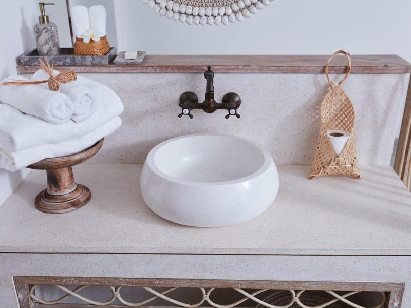 Jasna łazienka z okrągłą umywalką, ręcznikami i dekoracyjnym koszem na drewnianej półce.