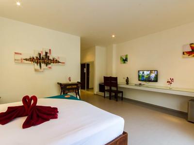 Helles Zimmer mit großem Bett, Schreibtisch, Wandregal, Dekorationen und Fernseher an der Wand.