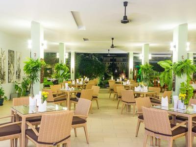 Großer, heller Speisesaal mit vielen Tischen, Stühlen und grünen Pflanzen in modernen weißen Säulen.