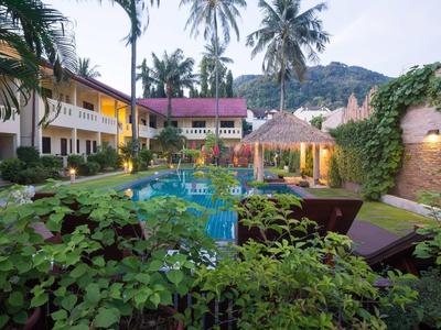 Hotelgarten mit Pool, Palmen, Liegestühlen und Pflanzen in tropischer Umgebung bei Dämmerung.