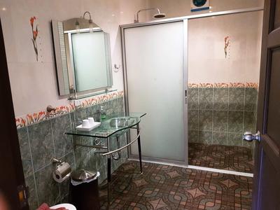 Kleines Bad mit Glaswaschbecken, Spiegel, Duschkabine und grün gemusterten Fliesen.