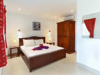 Helles Schlafzimmer mit großem Holzbett, Nachttischen, Holzkleiderschrank und roten Vorhängen.