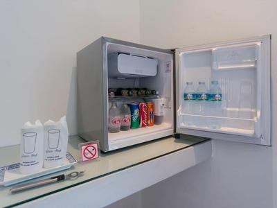 Kleiner grauer Kühlschrank mit Getränken wie Wasser, Cola und Milch, daneben Besteck und Becher.