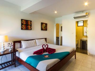 Helles Zimmer mit Doppelbett, dekorativen Handtüchern, Nachttisch, Lampe und Zugang zum Bad.