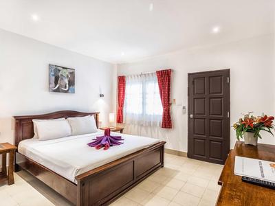 Helles Schlafzimmer mit großem Holzbett, roten Vorhängen und Blumendekoration auf Kommode.