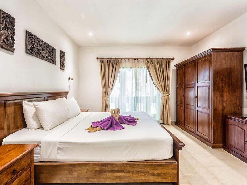 Hell eingerichtetes Schlafzimmer mit Holzmöbeln und dekorativ gefalteten Handtüchern auf dem Bett.