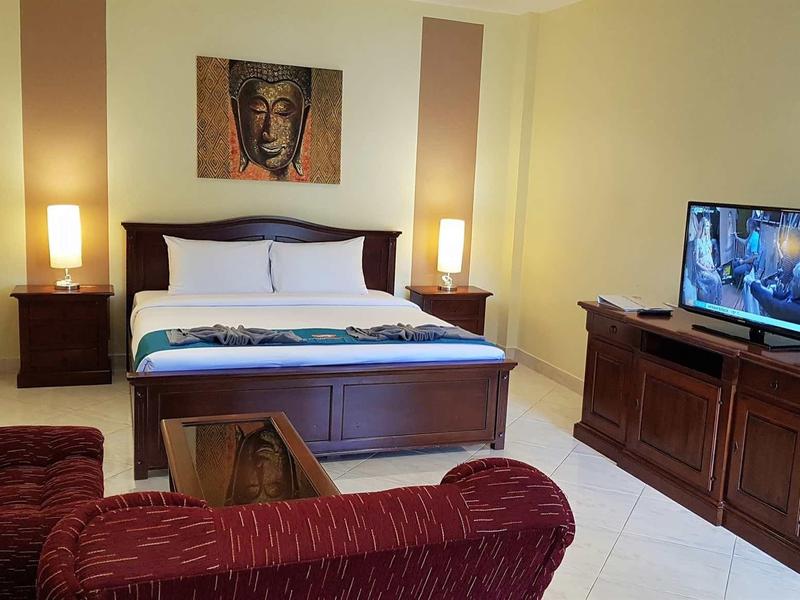 Gemütliches Wohnzimmer mit rotem Sofa, Holzmöbeln und Fernseher auf Sideboard, Wandbild über Bett.