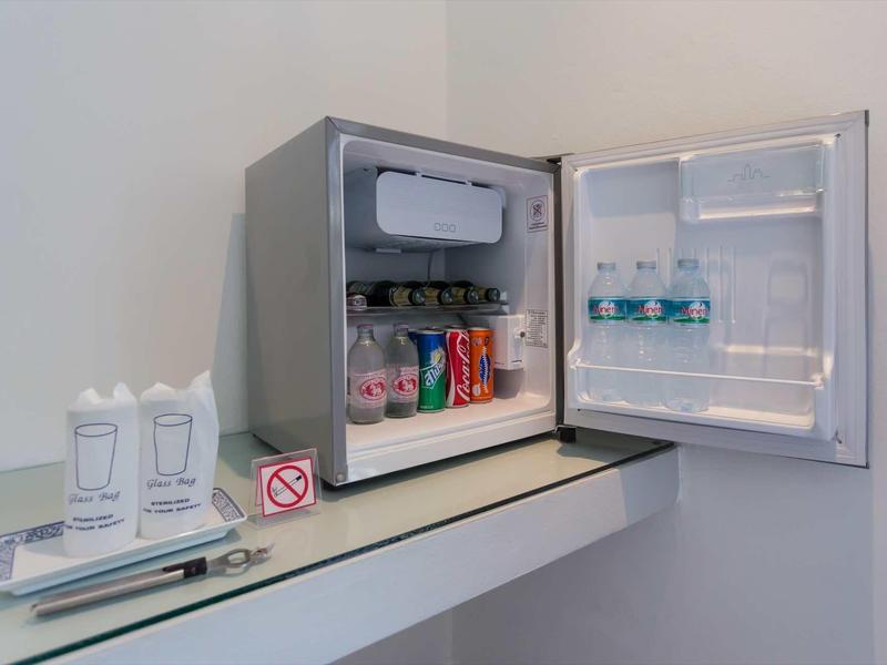 Kleiner grauer Kühlschrank mit Getränken wie Wasser, Cola und Milch, daneben Besteck und Becher.