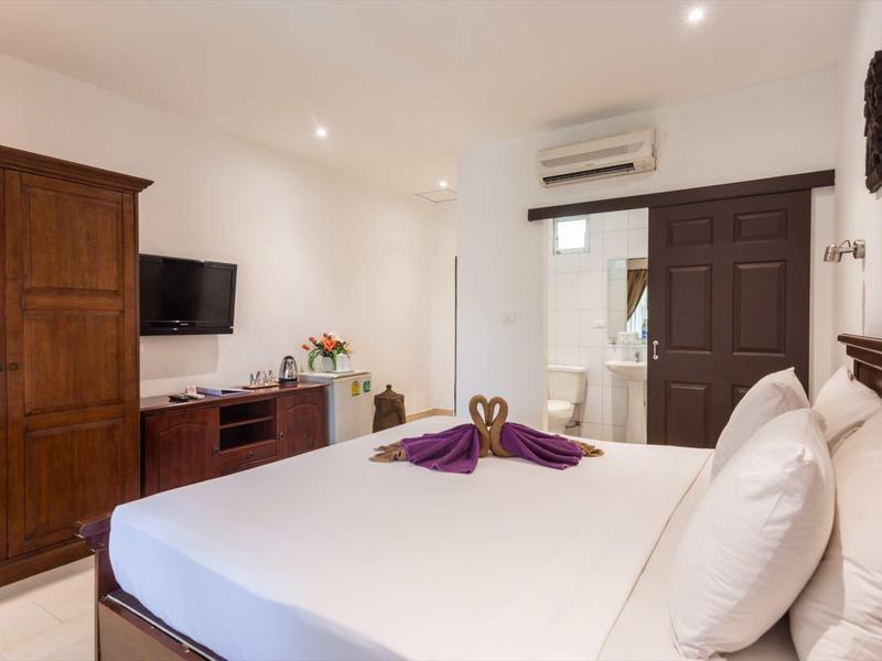 Schlafzimmer mit großem Bett, Holzmöbeln, Wandfernseher und dekorativen Handtüchern in Herzform.