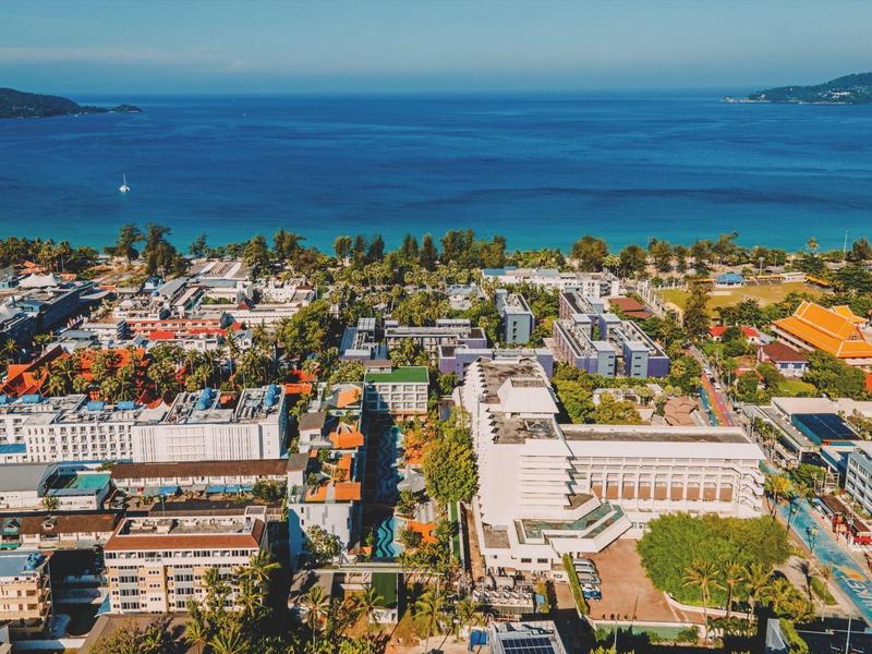 Vista aerea di una città costiera con hotel e mare azzurro sotto un cielo sereno.