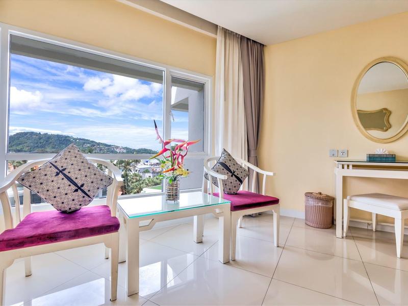 Angolo luminoso della camera d'hotel con finestra, cuscini colorati e vista sulle colline verdi.