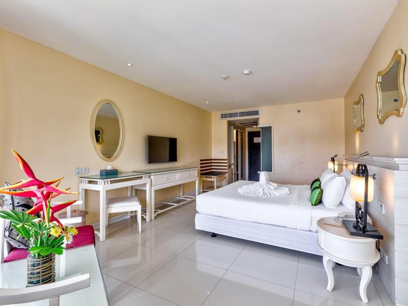 Camera d'hotel moderna con letto matrimoniale, scrivania, TV e composizione floreale vicino alla finestra.