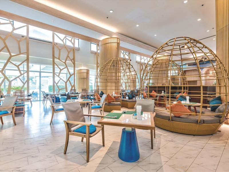 Area lounge moderna dell'hotel con grandi finestre, comode poltrone e sedute decorative a cupola.