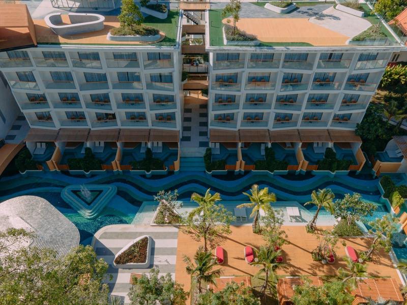 Vista di un hotel moderno con piscina e terrazza, circondato da alberi e piante.