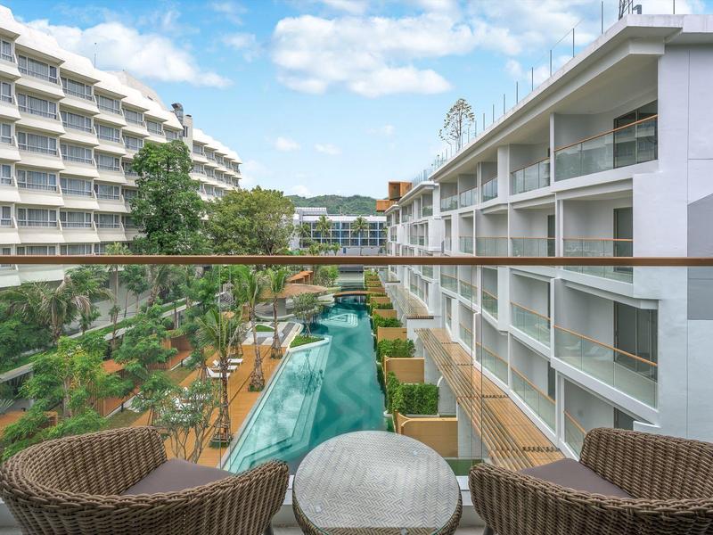 Vista di una piscina d'hotel tra due edifici moderni con sedie e tavolo sul balcone.