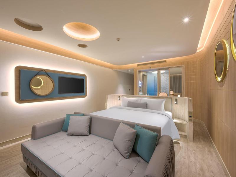 Camera d'hotel moderna con letto, divano e illuminazione indiretta.