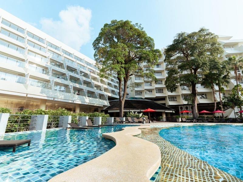 Grande piscina dell'hotel con sdraio circostanti e alberi sotto un cielo limpido.
