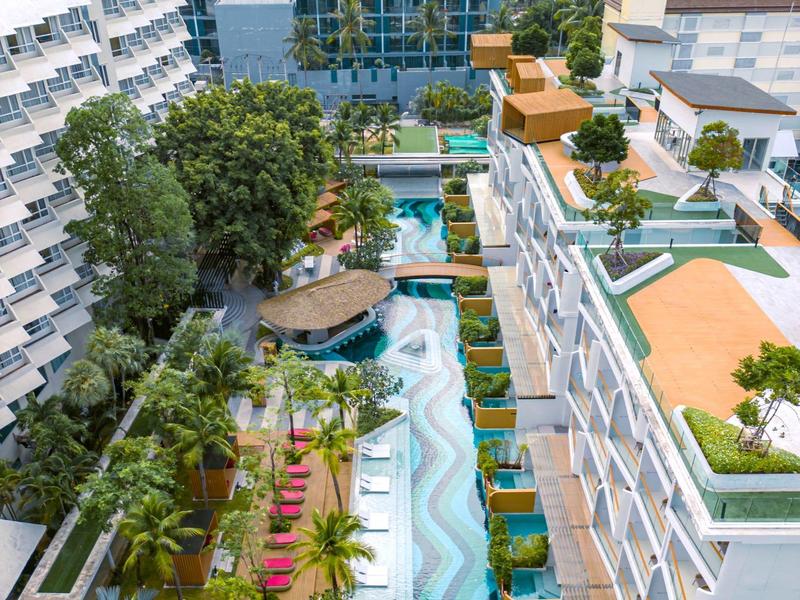 Vista di un hotel con piscina, lettini e una città sullo sfondo.