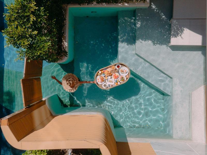 Piscina con due lettini, un albero ombreggiato e un vassoio con cibo e bevande.