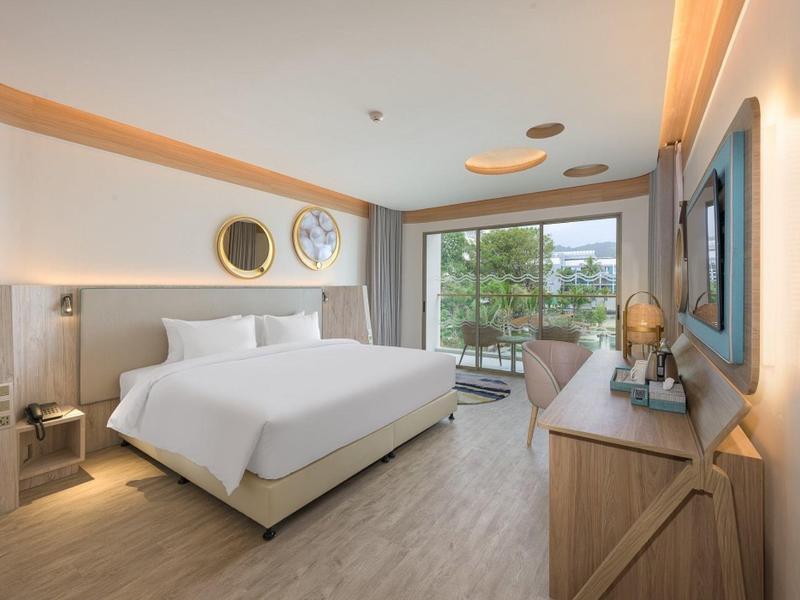 Camera d'hotel moderna con letto grande, pavimento in legno e balcone con vista su alberi verdi.