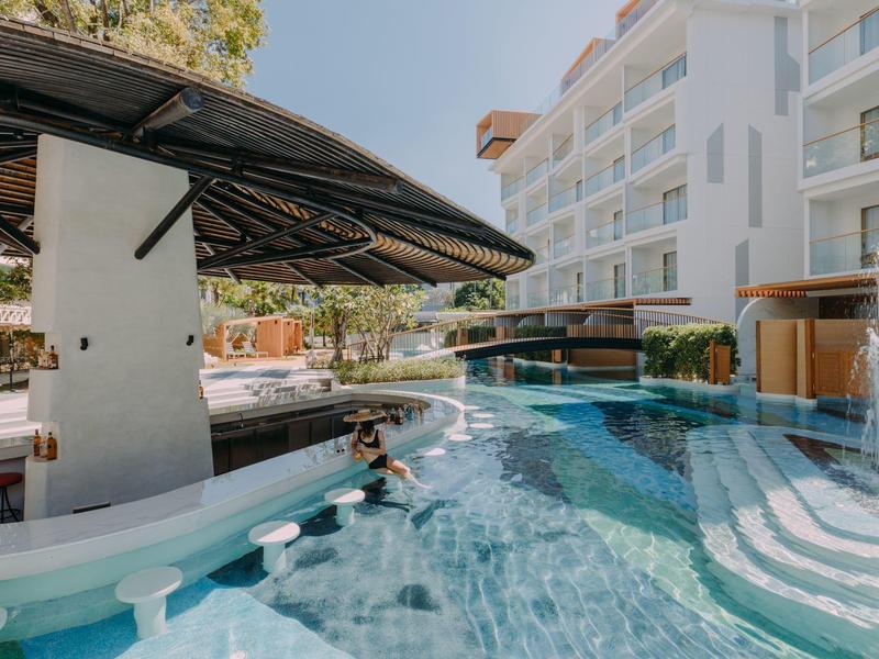 Area piscina con bar in acqua e posti a sedere in un complesso alberghiero sotto un cielo azzurro.