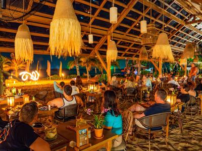 Levendige buitenbar met houten dak en tropische decoratie 's nachts.