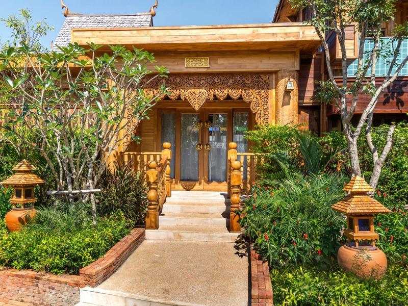 Ingang naar een hotel met traditioneel houten ontwerp en groene planten aan beide zijden van het pad.